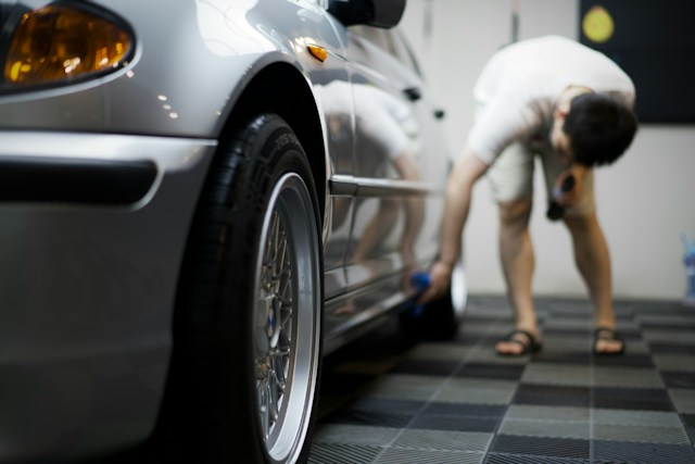 Silver metallic car in a garage, with someone cleaning the paintwork along its side in the background